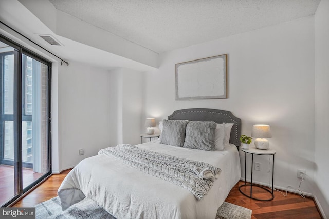 bedroom with access to outside, a textured ceiling, visible vents, and wood finished floors