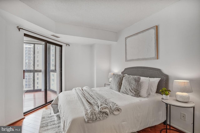 bedroom featuring access to outside, a textured ceiling, visible vents, and wood finished floors