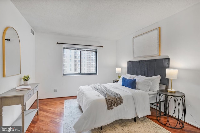 bedroom featuring light wood-style floors, visible vents, a textured ceiling, and baseboards