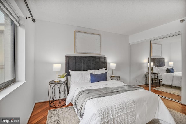 bedroom featuring a textured ceiling, a closet, wood finished floors, and baseboards