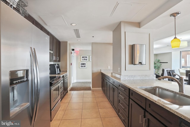 kitchen with light stone counters, stainless steel appliances, a sink, hanging light fixtures, and dark brown cabinets