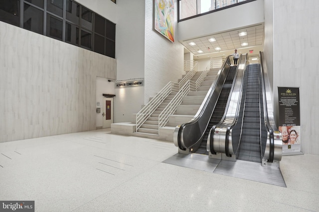 staircase featuring elevator, a towering ceiling, and speckled floor