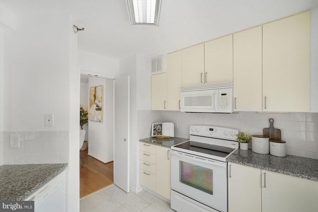 kitchen with cream cabinets, white appliances, visible vents, dark stone counters, and tasteful backsplash