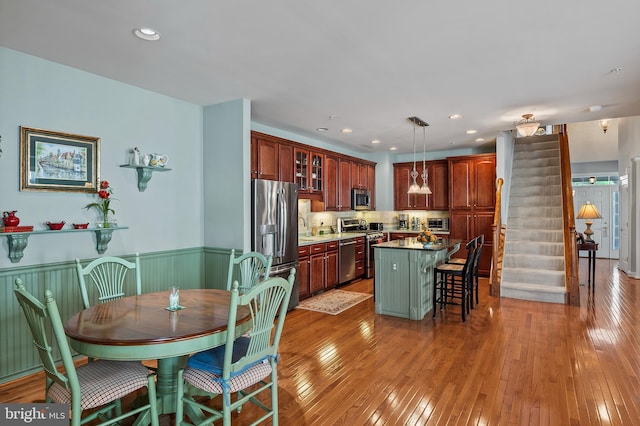 kitchen featuring a center island, a wainscoted wall, light wood finished floors, appliances with stainless steel finishes, and a kitchen bar