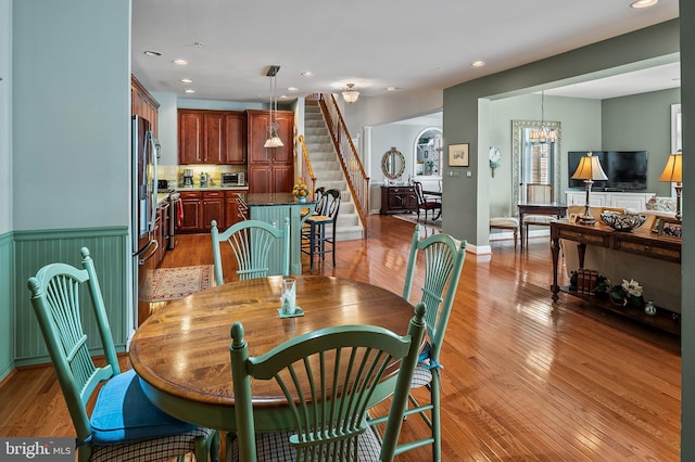 dining area featuring a wainscoted wall, stairs, light wood-type flooring, a notable chandelier, and recessed lighting