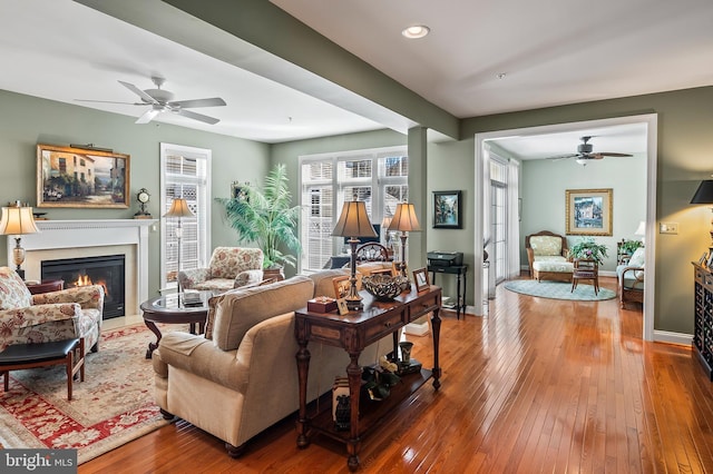 living area with wood-type flooring, baseboards, ceiling fan, and a fireplace with flush hearth