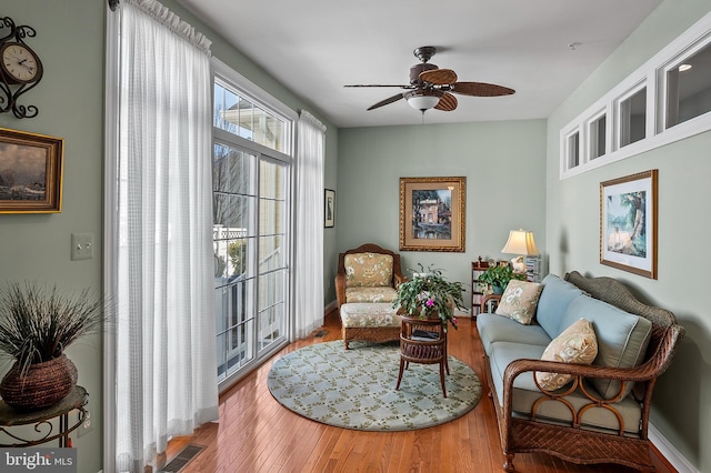 living area with a ceiling fan, visible vents, and wood finished floors