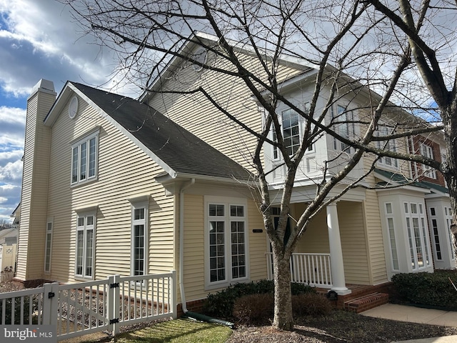 view of property exterior featuring covered porch, a chimney, fence, and roof with shingles