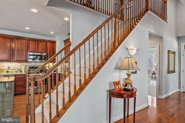 staircase featuring a high ceiling, baseboards, wood finished floors, and recessed lighting