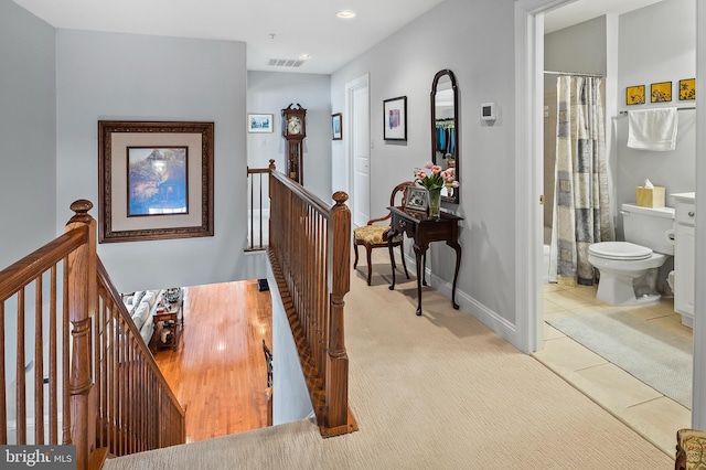 hall with visible vents, baseboards, tile patterned floors, carpet, and an upstairs landing