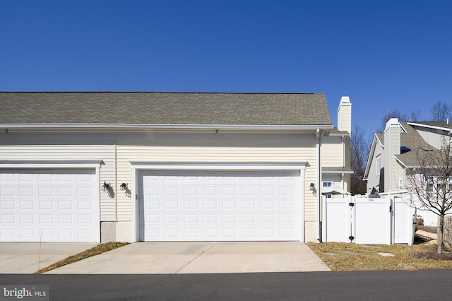 garage with concrete driveway, fence, and a gate