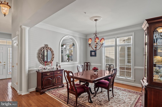 dining area featuring crown molding, an inviting chandelier, wood finished floors, and ornate columns