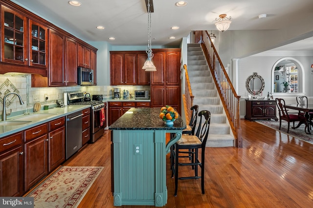 kitchen featuring reddish brown cabinets, hardwood / wood-style flooring, stainless steel appliances, a kitchen bar, and a sink