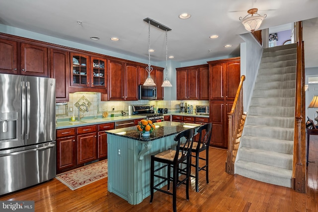 kitchen featuring a center island, dark wood-style flooring, stainless steel appliances, decorative backsplash, and a sink