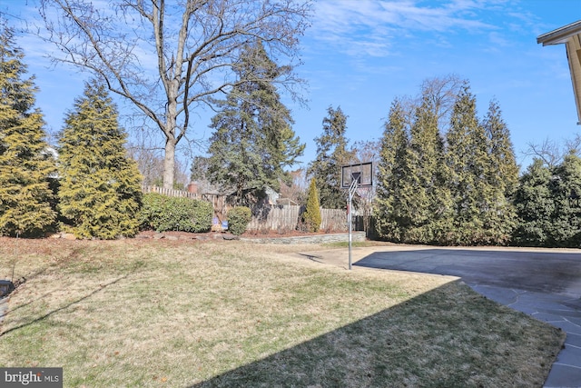 view of yard with basketball hoop and fence