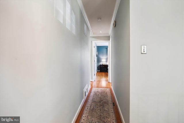 corridor with ornamental molding, wood finished floors, visible vents, and baseboards