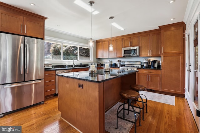 kitchen featuring brown cabinetry, a kitchen island, dark stone countertops, hanging light fixtures, and stainless steel appliances