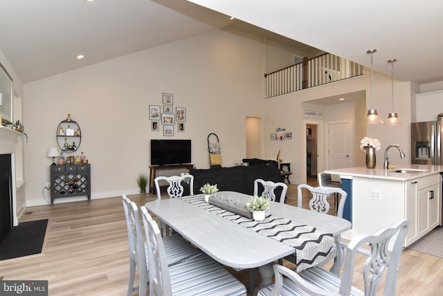 dining room with light wood finished floors, recessed lighting, a fireplace with flush hearth, high vaulted ceiling, and baseboards