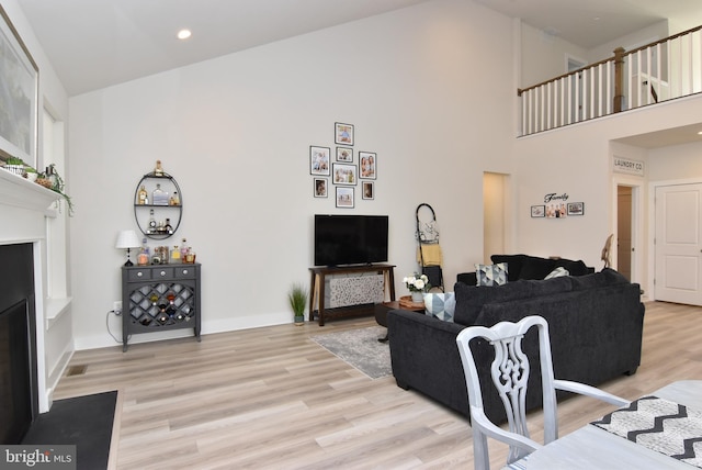 living area with recessed lighting, light wood-style flooring, a high ceiling, a fireplace with flush hearth, and baseboards