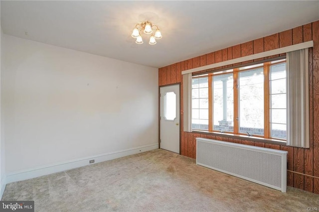 entryway with a notable chandelier, wooden walls, radiator heating unit, and light colored carpet