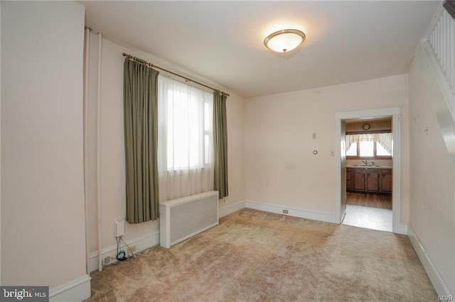 spare room with light carpet, radiator heating unit, baseboards, and a sink