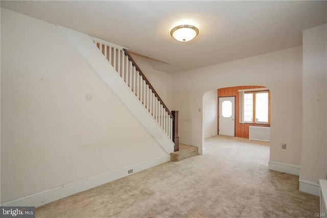 foyer with arched walkways, baseboards, radiator, stairway, and carpet floors