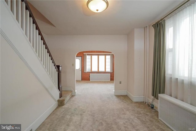 entrance foyer with arched walkways, light carpet, stairs, and radiator