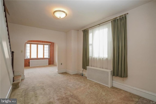 unfurnished room featuring baseboards, light colored carpet, and radiator heating unit