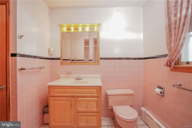 bathroom with toilet, a baseboard heating unit, vanity, tile walls, and wainscoting