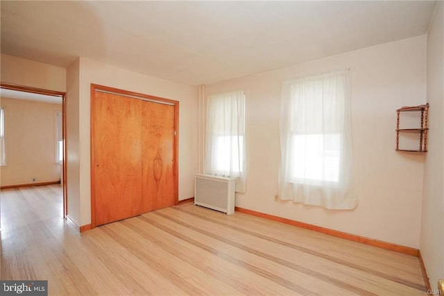 unfurnished bedroom featuring a closet, baseboards, light wood-style flooring, and radiator heating unit