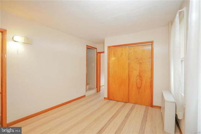 unfurnished bedroom with light wood-type flooring, a closet, baseboards, and radiator heating unit