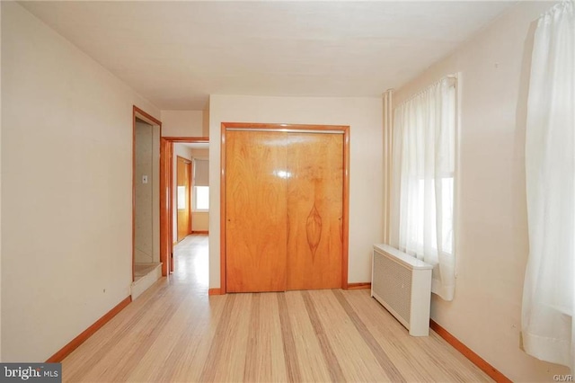 unfurnished bedroom with baseboards, light wood-style flooring, and radiator heating unit