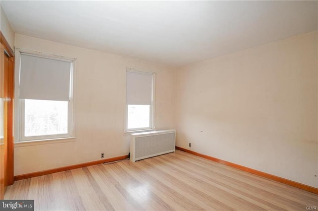 unfurnished room with light wood-style floors, baseboards, and radiator heating unit