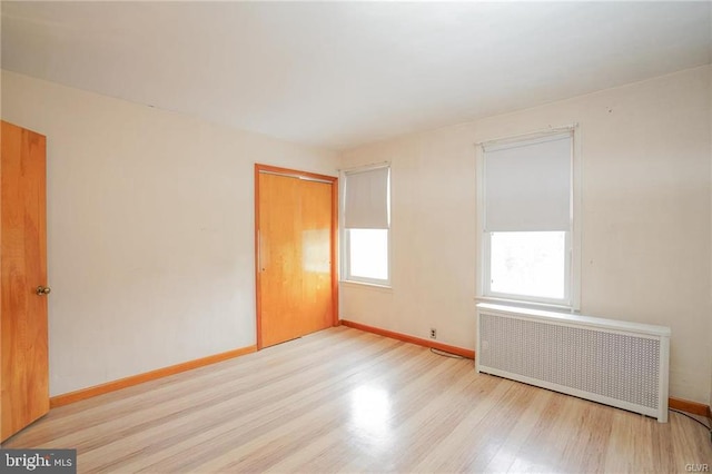 empty room featuring light wood finished floors, radiator heating unit, and baseboards