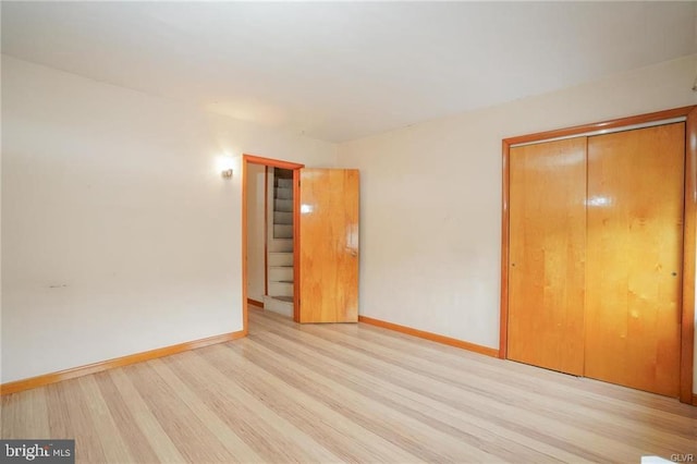 unfurnished bedroom with light wood-type flooring, a closet, and baseboards