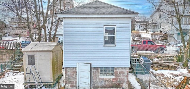 snow covered structure featuring an outbuilding, fence, and a storage unit