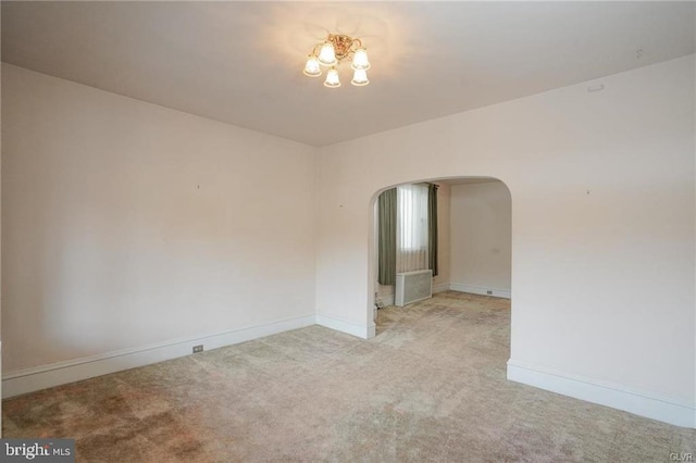 spare room featuring arched walkways, light carpet, and baseboards