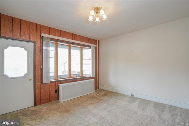 empty room with wooden walls, radiator heating unit, and light colored carpet