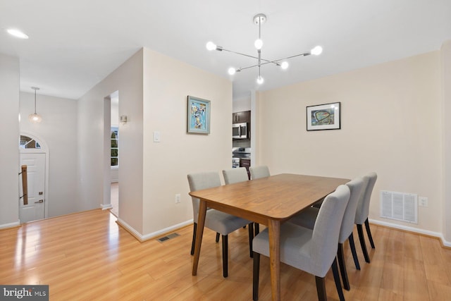 dining area with a chandelier, light wood-style flooring, visible vents, and baseboards