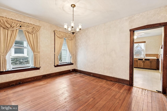 empty room with baseboards, hardwood / wood-style floors, and an inviting chandelier