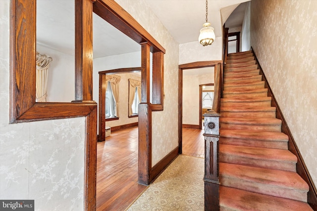 staircase featuring wallpapered walls, decorative columns, baseboards, and hardwood / wood-style flooring