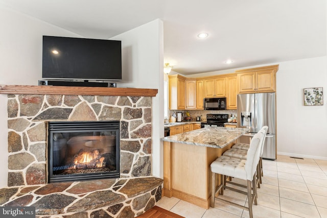 kitchen with light tile patterned floors, black appliances, light stone counters, and a fireplace