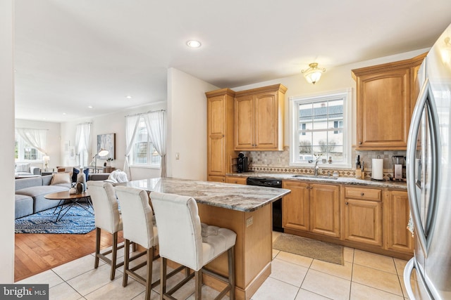 kitchen with a breakfast bar area, a sink, black dishwasher, backsplash, and freestanding refrigerator