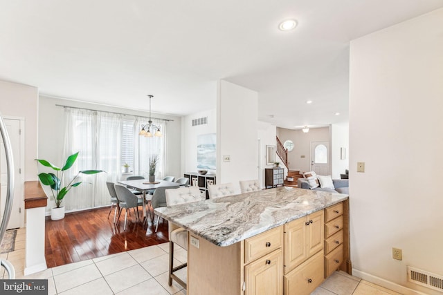 kitchen with light tile patterned floors, light brown cabinetry, visible vents, and a kitchen breakfast bar