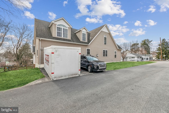 view of home's exterior featuring a shingled roof, fence, aphalt driveway, and a yard