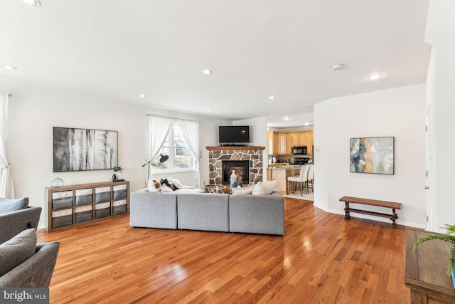 living room featuring recessed lighting, a fireplace, light wood-style flooring, and baseboards