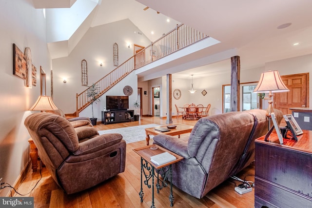 living area with baseboards, a towering ceiling, hardwood / wood-style flooring, stairway, and recessed lighting