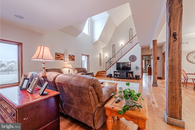 living area with light wood finished floors, stairway, a towering ceiling, and visible vents