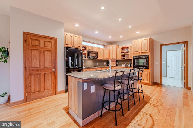 kitchen featuring light wood-style floors, a kitchen breakfast bar, dark stone countertops, black appliances, and a sink