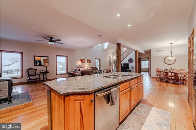 kitchen with dishwasher, open floor plan, a kitchen island with sink, stone counters, and a sink